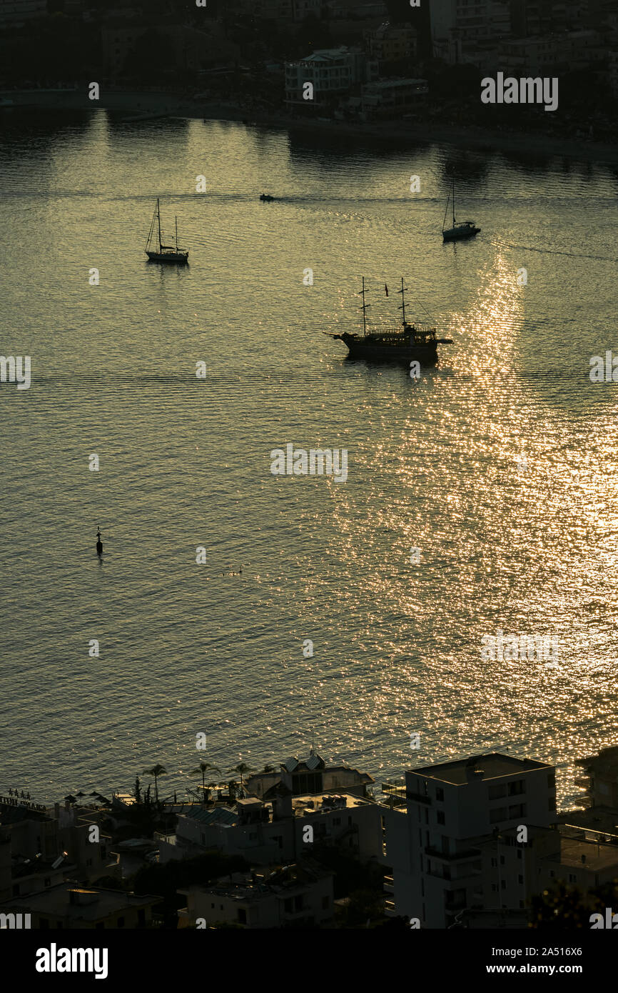 Low key aerial view of Saranda bay, Albania, in the Albanian riviera with setting Sun light reflections in the sea water and silhouettes of ships and boats in the bay Stock Photo