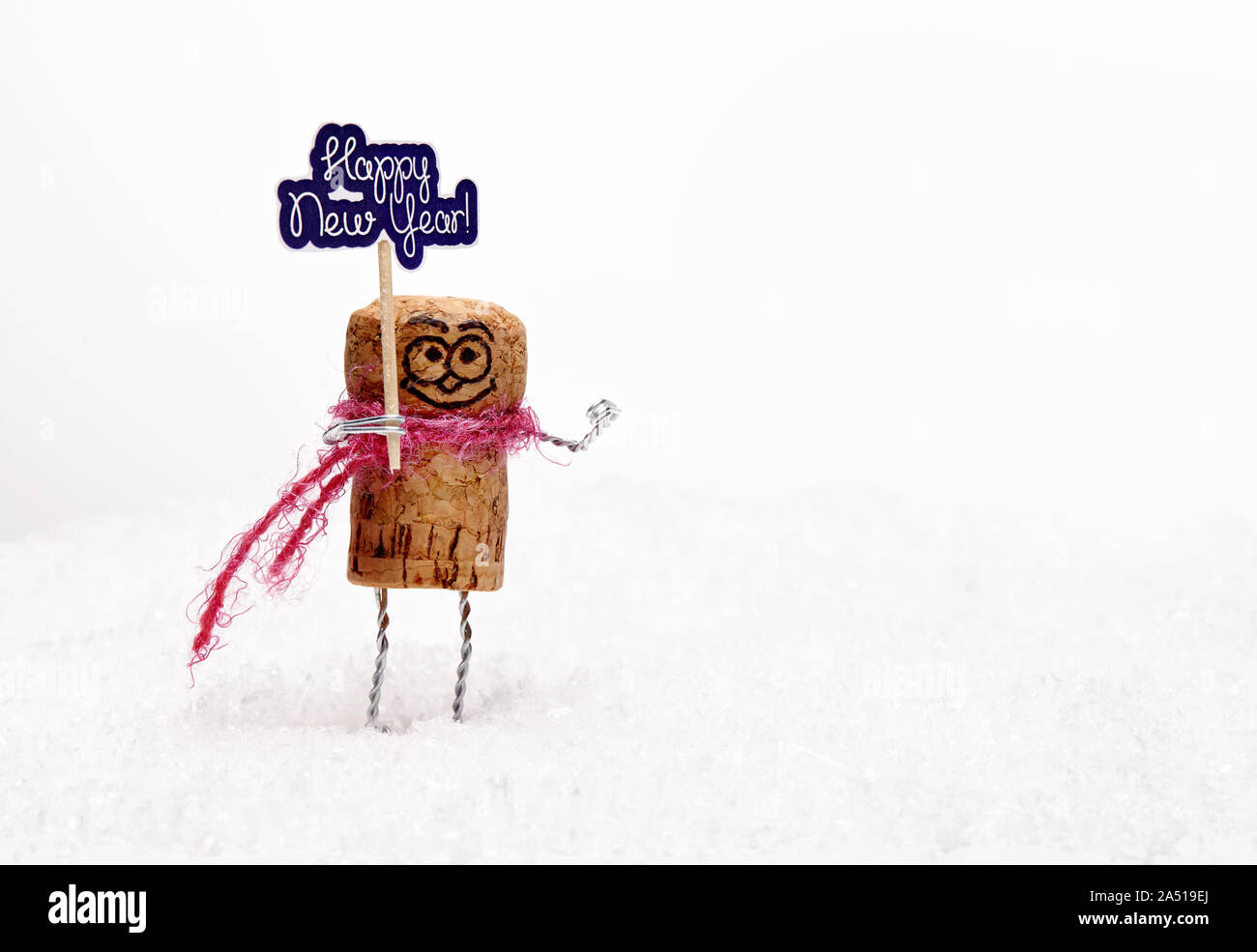 Funny wine cork manikin on white snow wishes anybody 'happy new year'. New Year composition with toys. Stock Photo