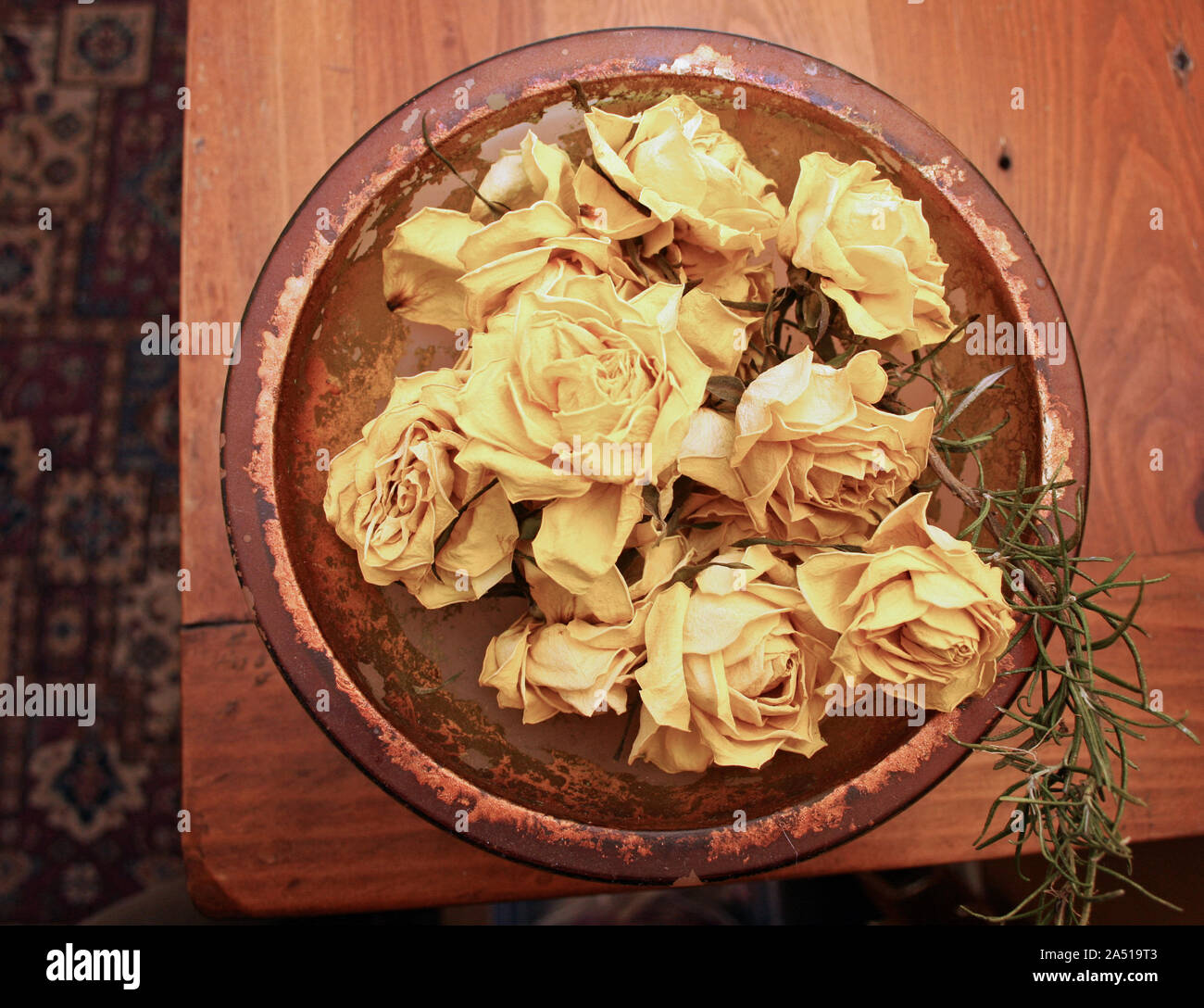 Dried yellow roses in glass bowl on a wooden table taken from above Stock Photo