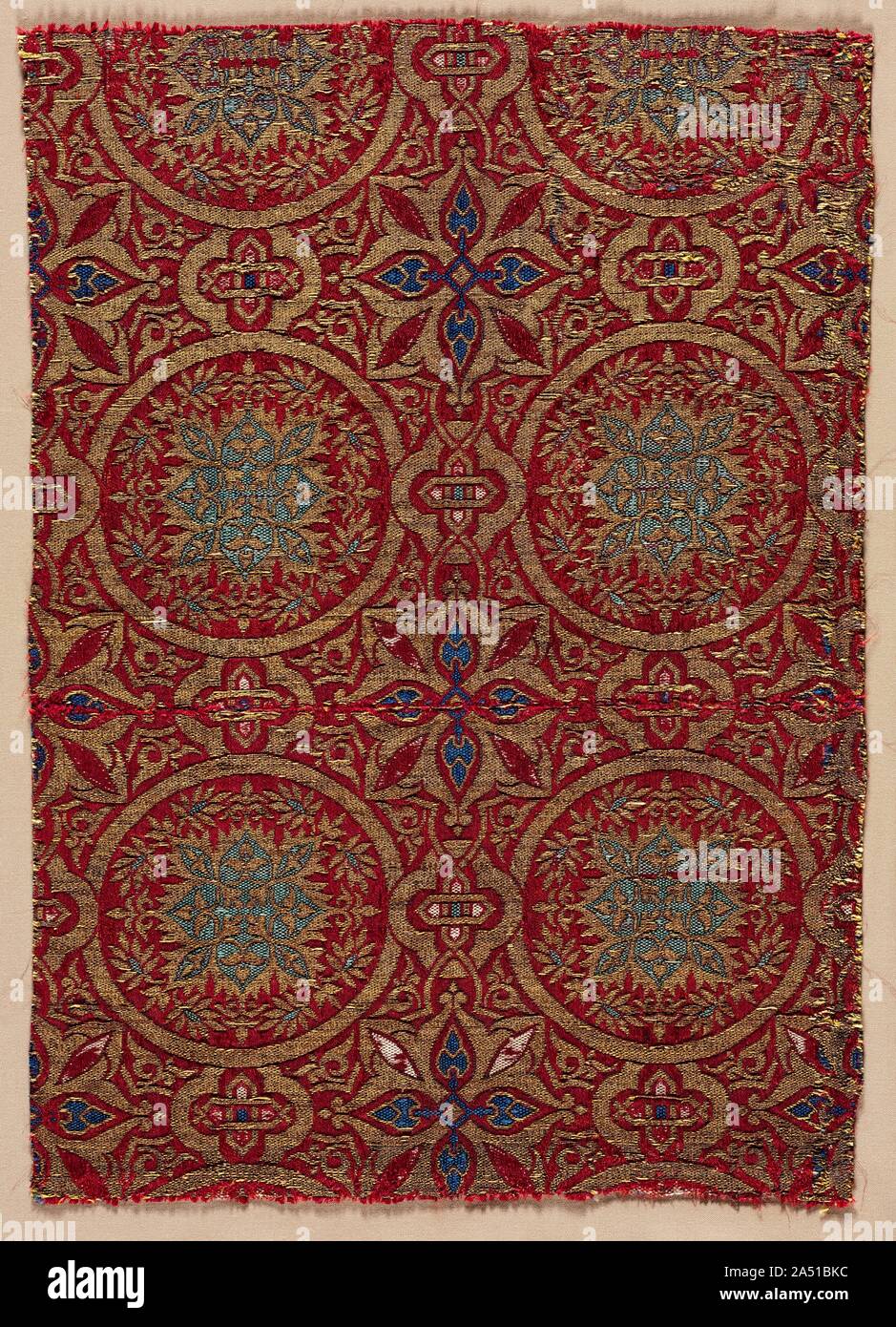Lampas with foliate roundels, 1300s. This textile shows the development of the Hispano-Moresque style in the 1300s. The bright green, blue, white, and gold design against a rich red ground produces a jewel-like quality that was not seen again after the end of the century. Stock Photo