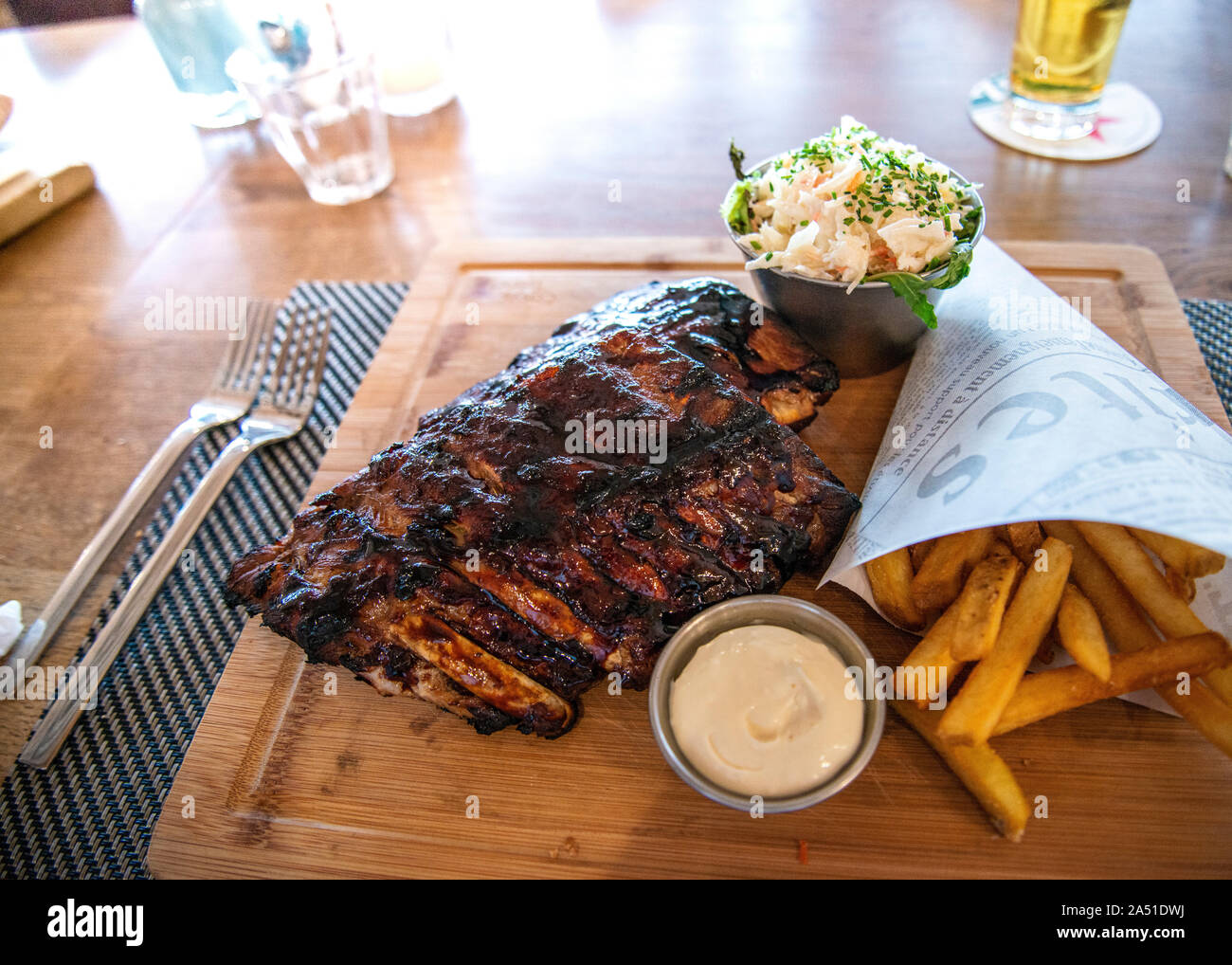 traditional rack of tasty mouthwatering bbq pork ribs served on wooden plate with hand cut chips and coleslaw, Stock Photo