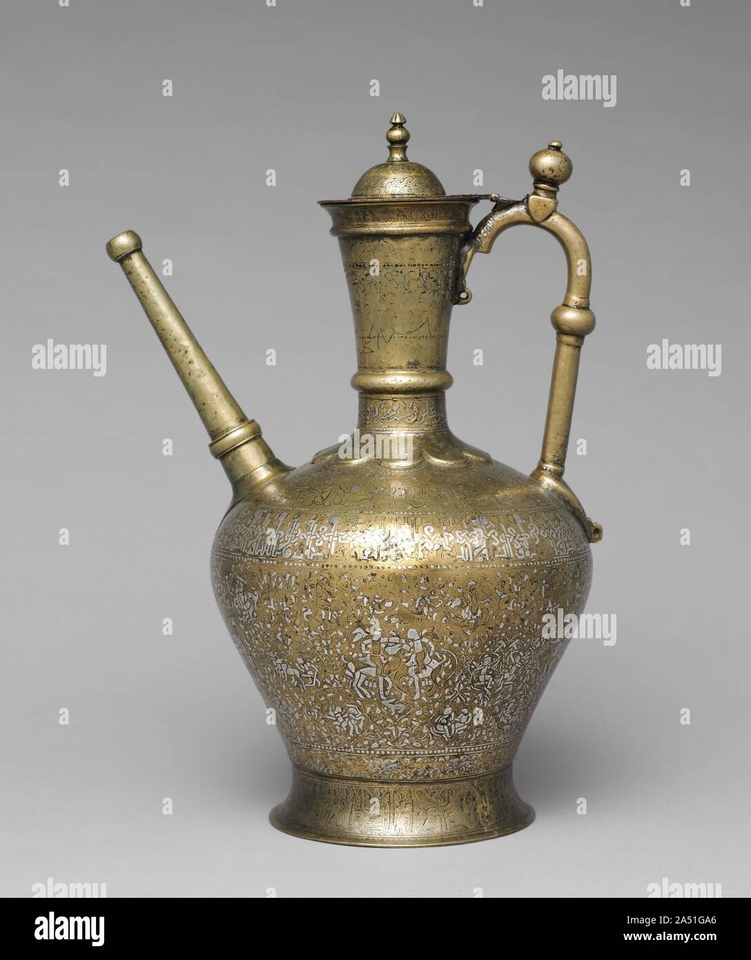 Luxury Ewer Extending Good Fortune to the Owner, 1223. The lavish silver inlaid surface features a wide band displaying medallions with scenes of court and daily life and an inscription band on the shoulder, written in plaited and animated kufic (angular) script, extending good fortune, generosity, and charitable giving to the owner. This celebrated ewer is dated 1223 and signed by the master craftsman Ahmad al-Dhaki of Mosul. Stock Photo
