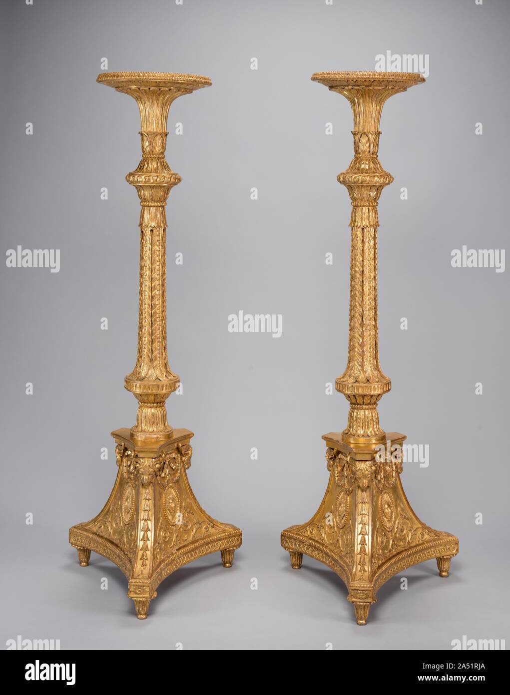 Pair of Candle Stands (torch&#xe8;res), c. 1773. Inspired by discoveries of ancient ruins at Herculaneum and Pompeii in the 1730s, fashionable aristocratic architecture and interiors reflected a taste for neoclassical decoration. Thomas Chippendale, the most recognizable, influential London cabinetmaker of this era made these candle stands as part of a larger suite of four for the grand drawing room of Brocket Hall, the country seat of Sir Peniston Lamb, a recently knighted English lord. Their design is modeled on an ancient Roman marble candlestick decorated with carved acanthus leaves, swags Stock Photo
