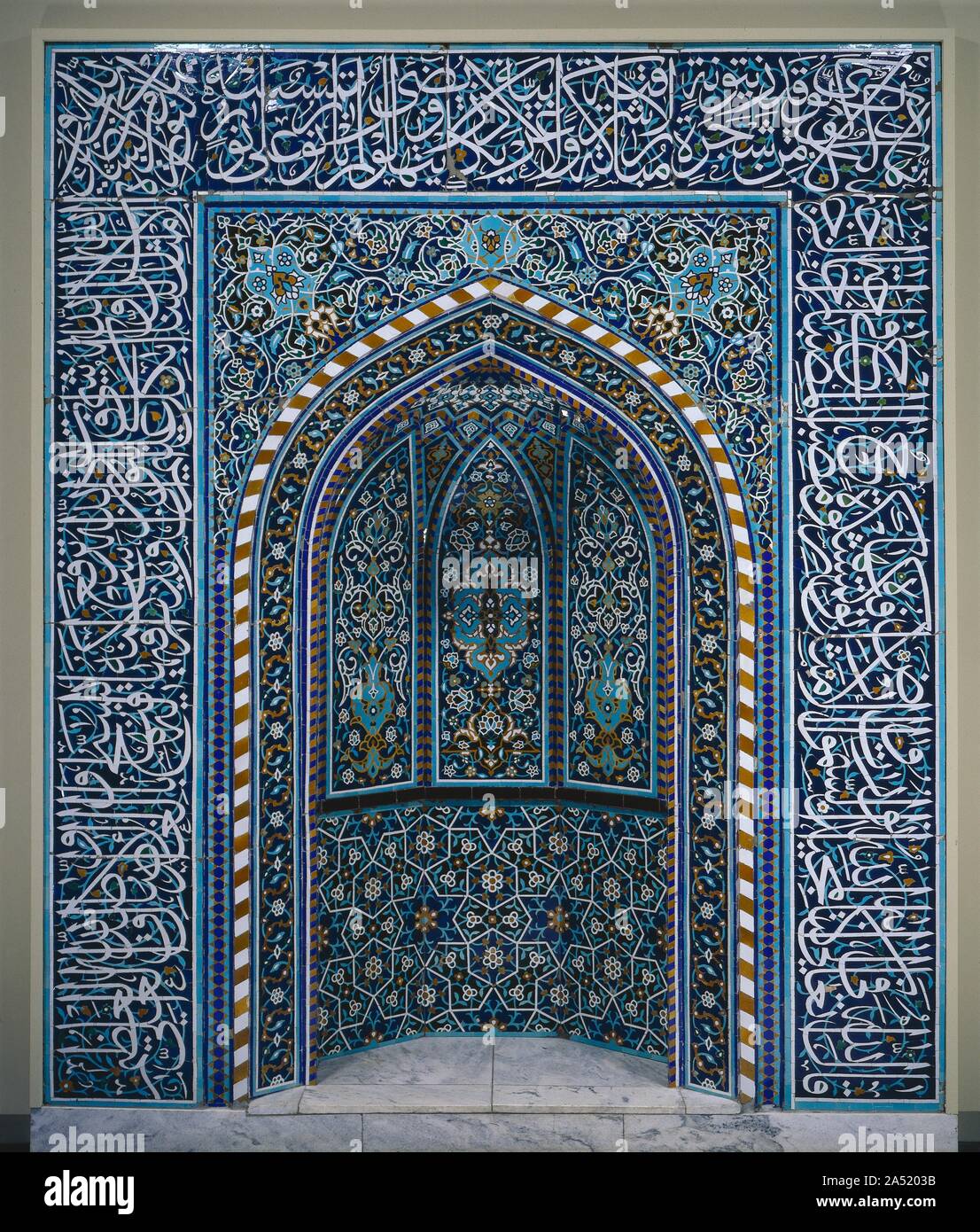 Prayer Niche (Mihrab), early 1600s. The prayer niche (mihrab in Arabic) is the focal point in the interior of a mosque. It is located in the qibla wall which is oriented toward Mecca, the holy city of Islam. Muslims face the qibla wall during prayer. This mihrab is an excellent example of different design elements-calligraphy, plants, and geometry-integrated into a beautiful harmonious whole. Graduated colours and sizes contribute to its success. The dominant white glaze presents the most important verses from the Qur&#x2019;an written in elegant thuluth script which frames the niche. White gl Stock Photo