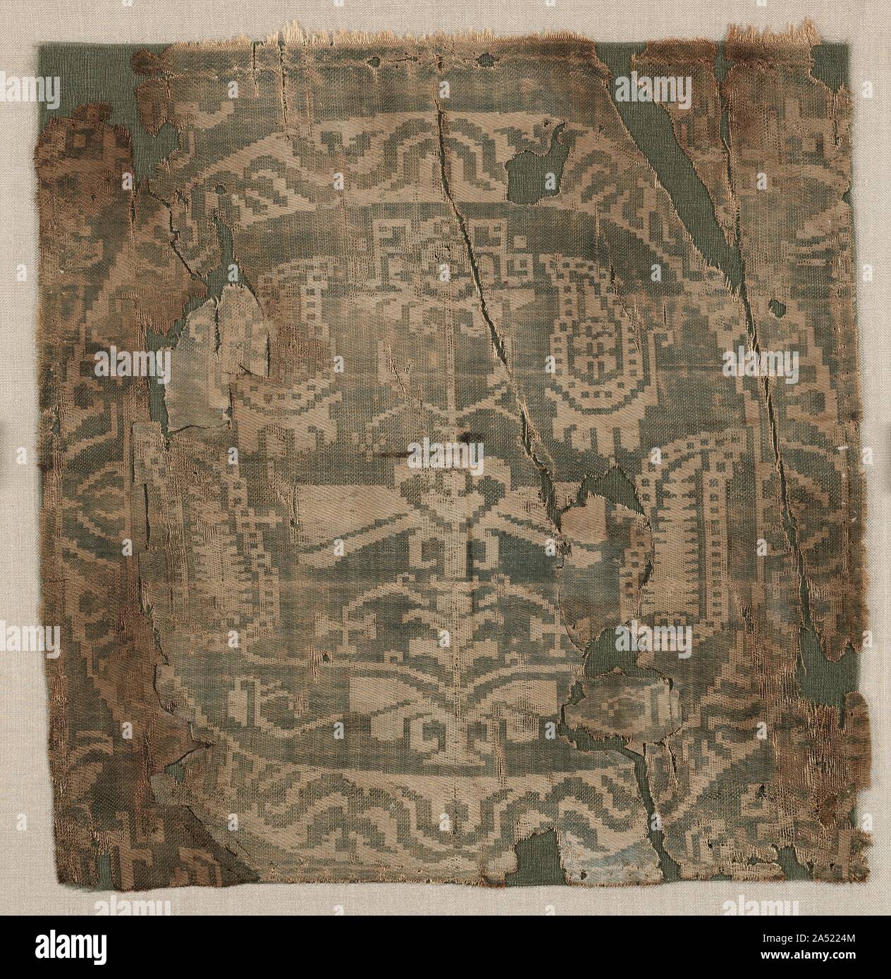 Roundel with angular palmette tree, from a tunic, 650-850. Four or six squares of this luxurious two-colour silk were originally sewn on a linen tunic, two positioned above the hemline in the front and two in the back, and possibly two more at the shoulder. The folded edges are still visible, including a silk sewing thread on the right side. The brittle condition is evident in the numerous crisp breaks. Stock Photo