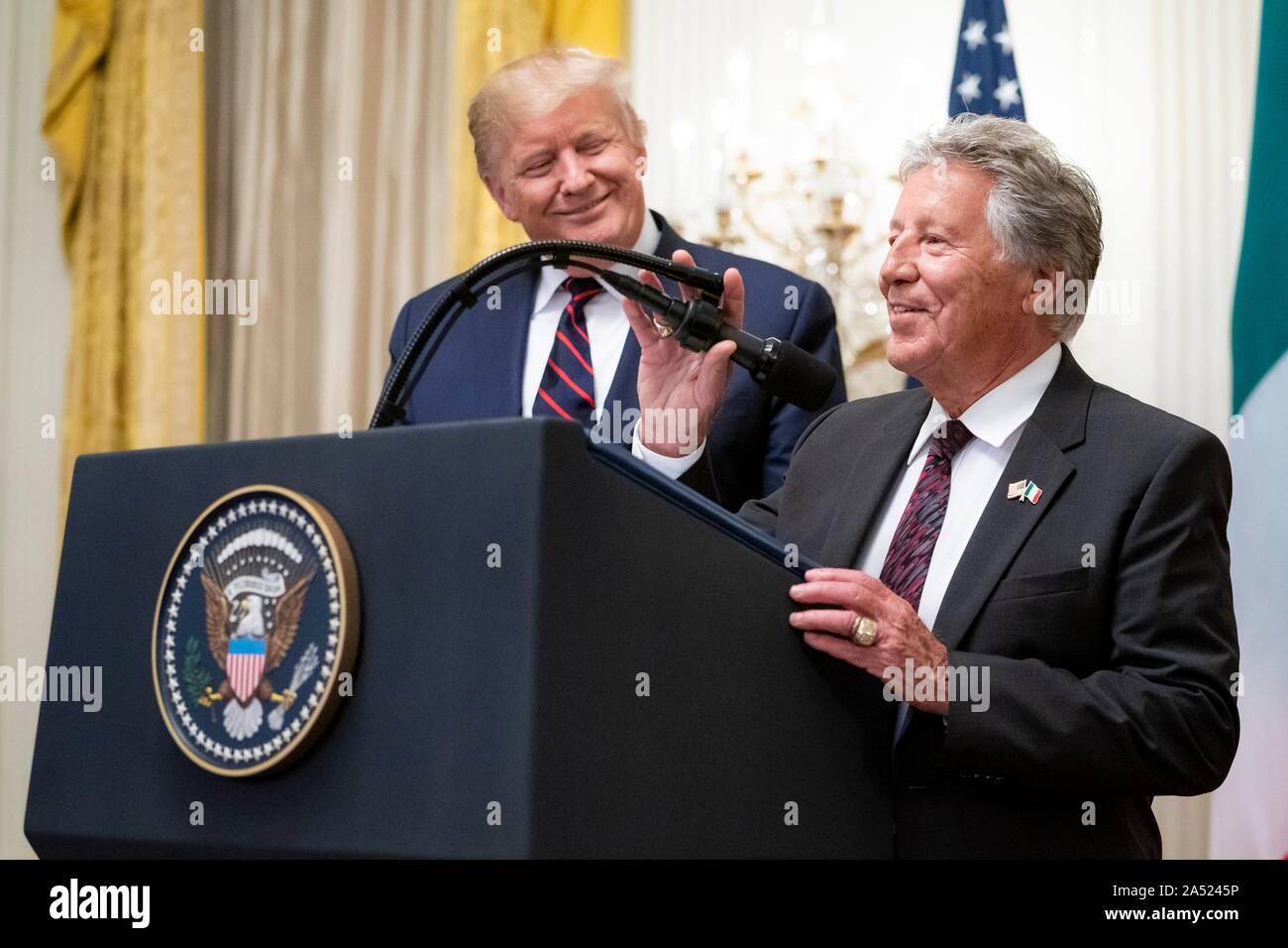 Washington, United States of America. 16 October, 2019. U.S President Donald Trump, left, smiles as he welcomes legendary race car driver Mario Andretti to the podium during a reception in honor of Italian President Sergio Mattarella in the East Room of the White House October 16, 2019 in Washington, DC. Credit: Tia Dufour/White House Photo/Alamy Live News Stock Photo