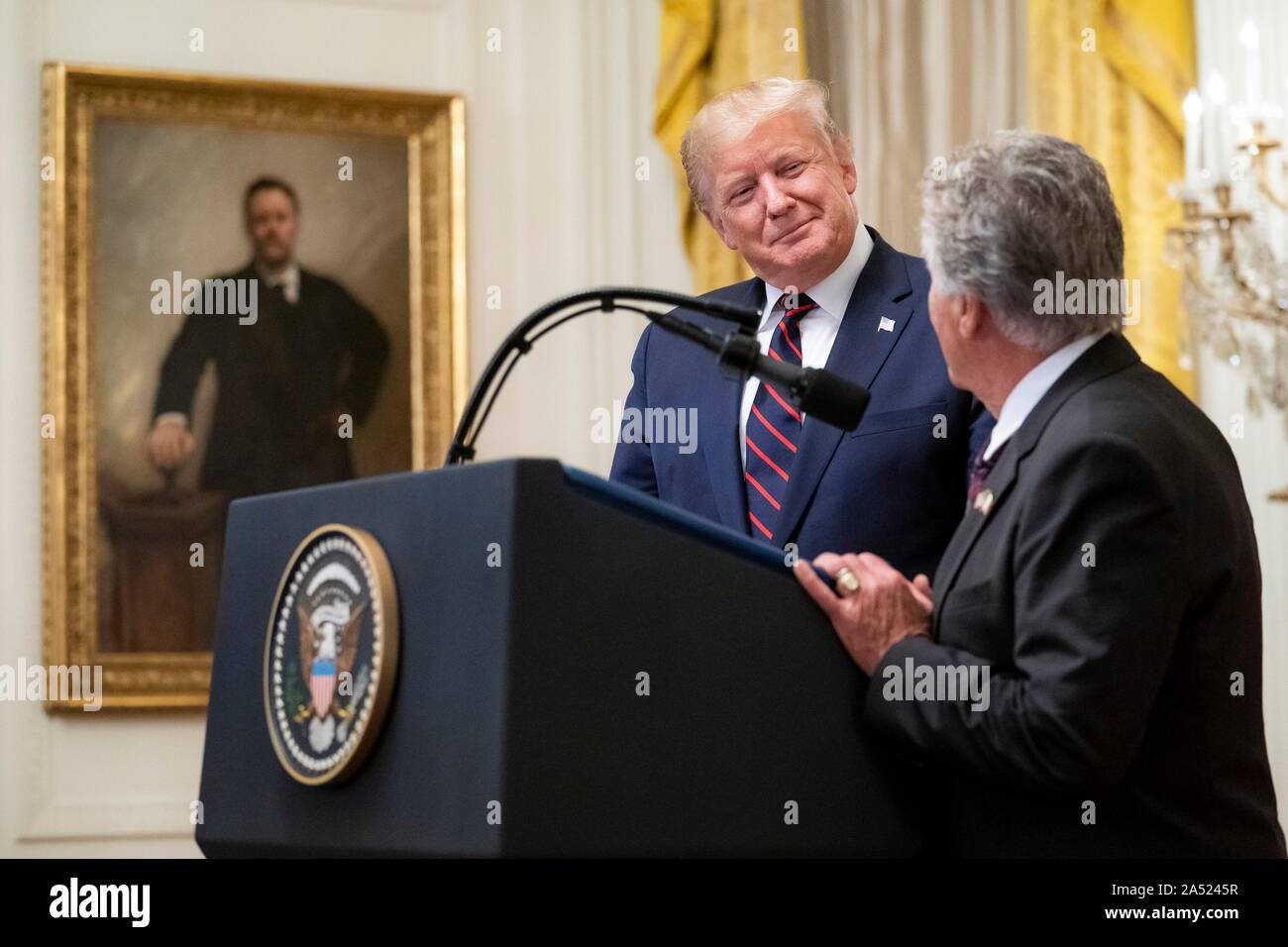 Washington, United States of America. 16 October, 2019. U.S President Donald Trump, left, smiles as he welcomes legendary race car driver Mario Andretti to the podium during a reception in honor of Italian President Sergio Mattarella in the East Room of the White House October 16, 2019 in Washington, DC. Credit: Tia Dufour/White House Photo/Alamy Live News Stock Photo