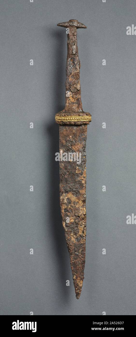 Single-Edged Knife (Scramasax), 600s. The scramasax, a single-edged knife, was a general purpose implement. It could serve equally well as a tool or as a weapon and generally did not exceed 12 inches in length. As with most objects of the Migration period, iron weapons survive as excavated grave goods and tend to be heavily corroded. The grips, now missing, were probably fashioned from wood or bone and silver inlay decorated the pommels (the knob on the hilt, or handle). The ornamental gold foil bands, perhaps from the original scabbards (the cases in which the blades of swords or daggers are Stock Photo