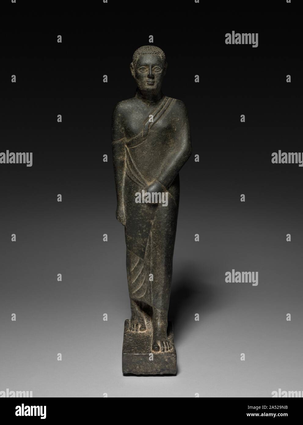 Statue of a Man, 200-100 BC or later. This striding figure represents a very late development in Egyptian sculpture and a fascinating combination of old and new. In keeping with contemporary fashion, he is draped in a three-part costume consisting of a T-shirt, wraparound skirt, and shawl. Also new is the naturalistic rendering of the man's real hair, here accompanied by a full beard. Entirely traditional, however, are the striding pose, the use of a back pillar, and the way the curves of the body show through the tightly wrapped garments. Stock Photo