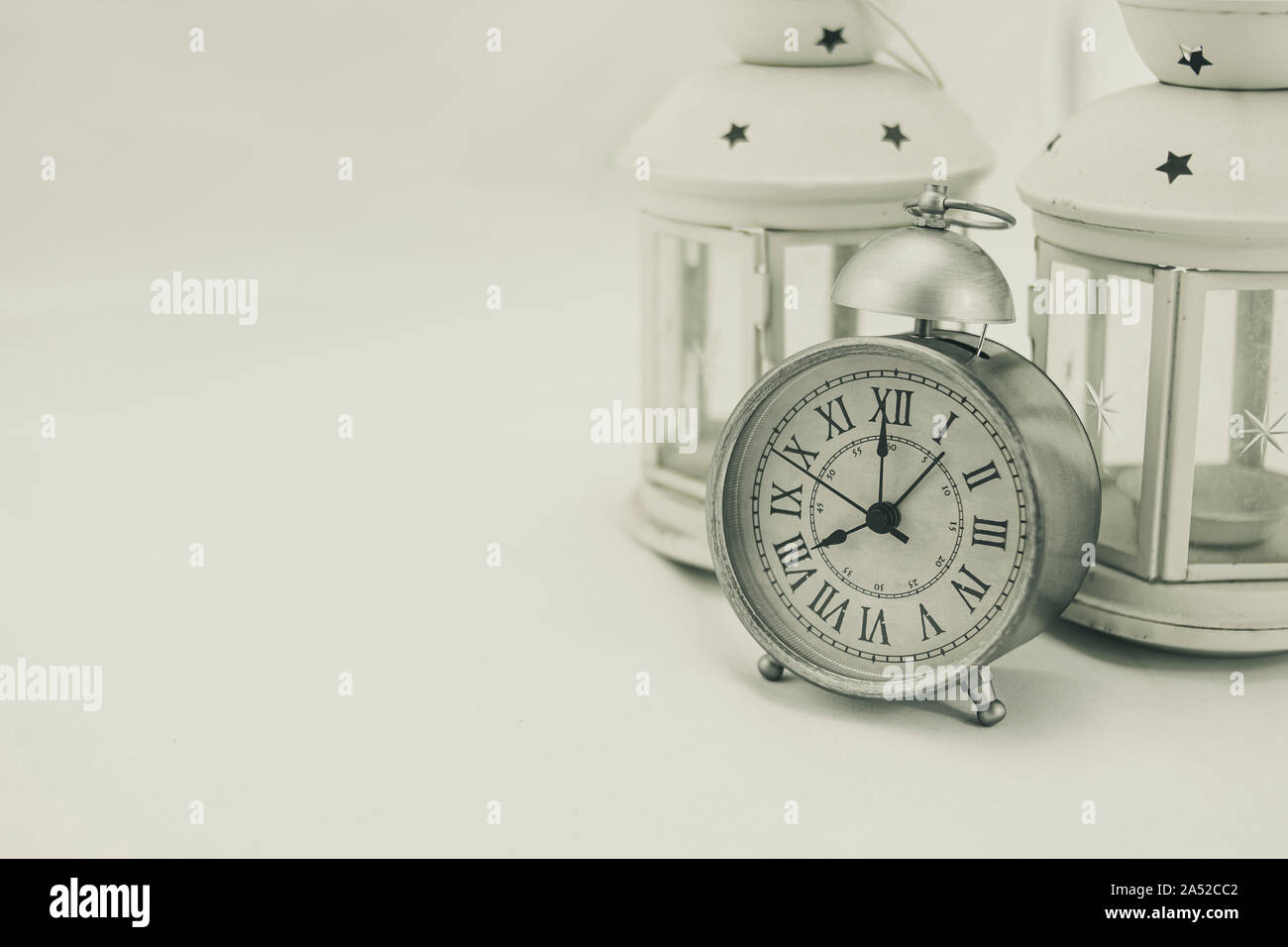 Classic gray alarm clock with two white lanterns candle holders on white background Stock Photo