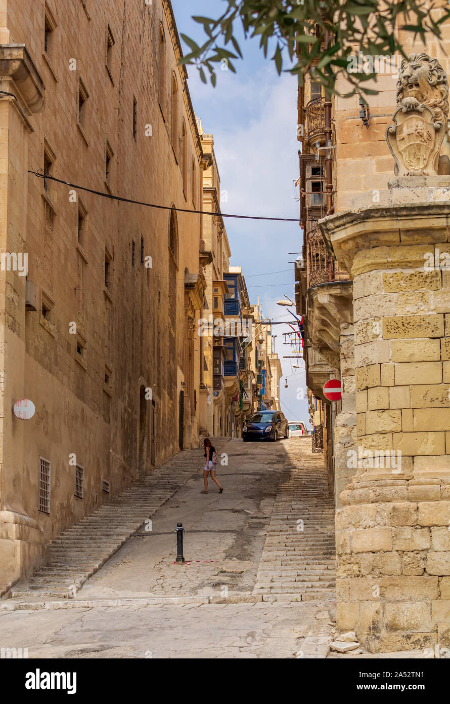 Young girl crossing typical Valletta street with rising road with stairs and traditional Maltese wooden balconies in the distance. Stock Photo