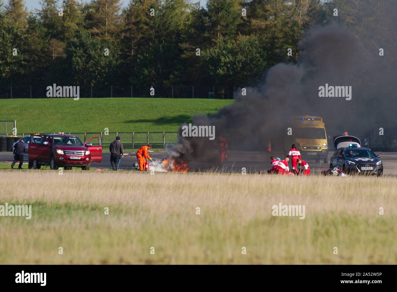 Dalton on Tees, England, 12 October 2019. Doctors treating a rider as marshalls extinguish a bike fire after a crash on the first lap of a Racebuykz.com Cup 1000 race during a No Limits meeting at Croft Circuit. Stock Photo