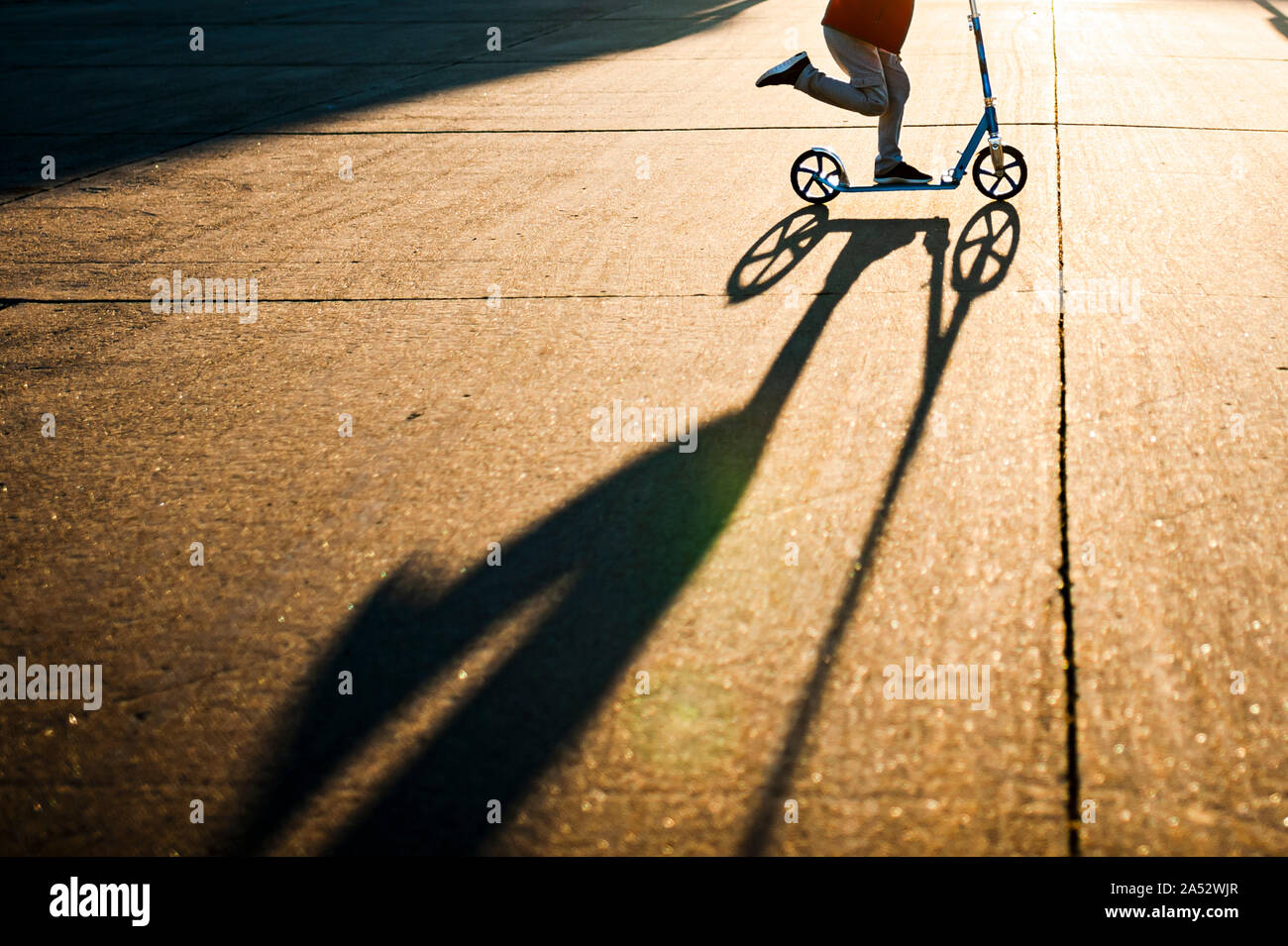 Lower half of boy scootering fast in sunlight with shadow in street Stock Photo