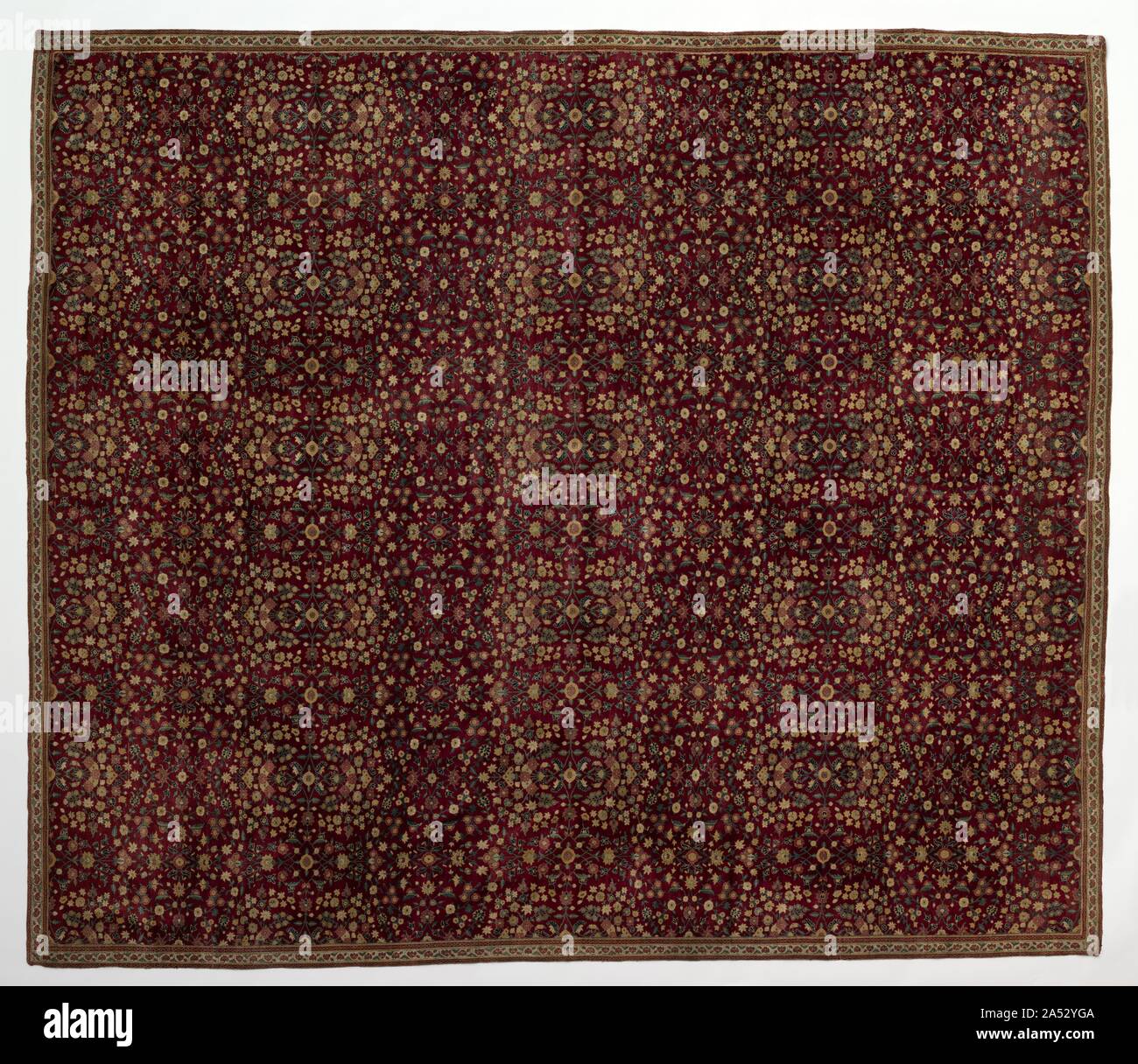 Woolen carpet with millefleurs decoration, early 1600s. This tour de force of Mughal weaving sets symmetrically intertwined flowering vines against a deep wine-red ground. The small-scale flowers that fill the ground space appear to be so numerous that this type of pattern is given the name millefleurs, &quot;thousand flowers&quot; in French, after a type of medieval European tapestry pattern. The use of pashmina wool indicates that this work was made in Kashmir, near the foothills of the Himalayas in northern India. They lend a silken sheen that augments the carpet&#x2019;s luxurious quality. Stock Photo