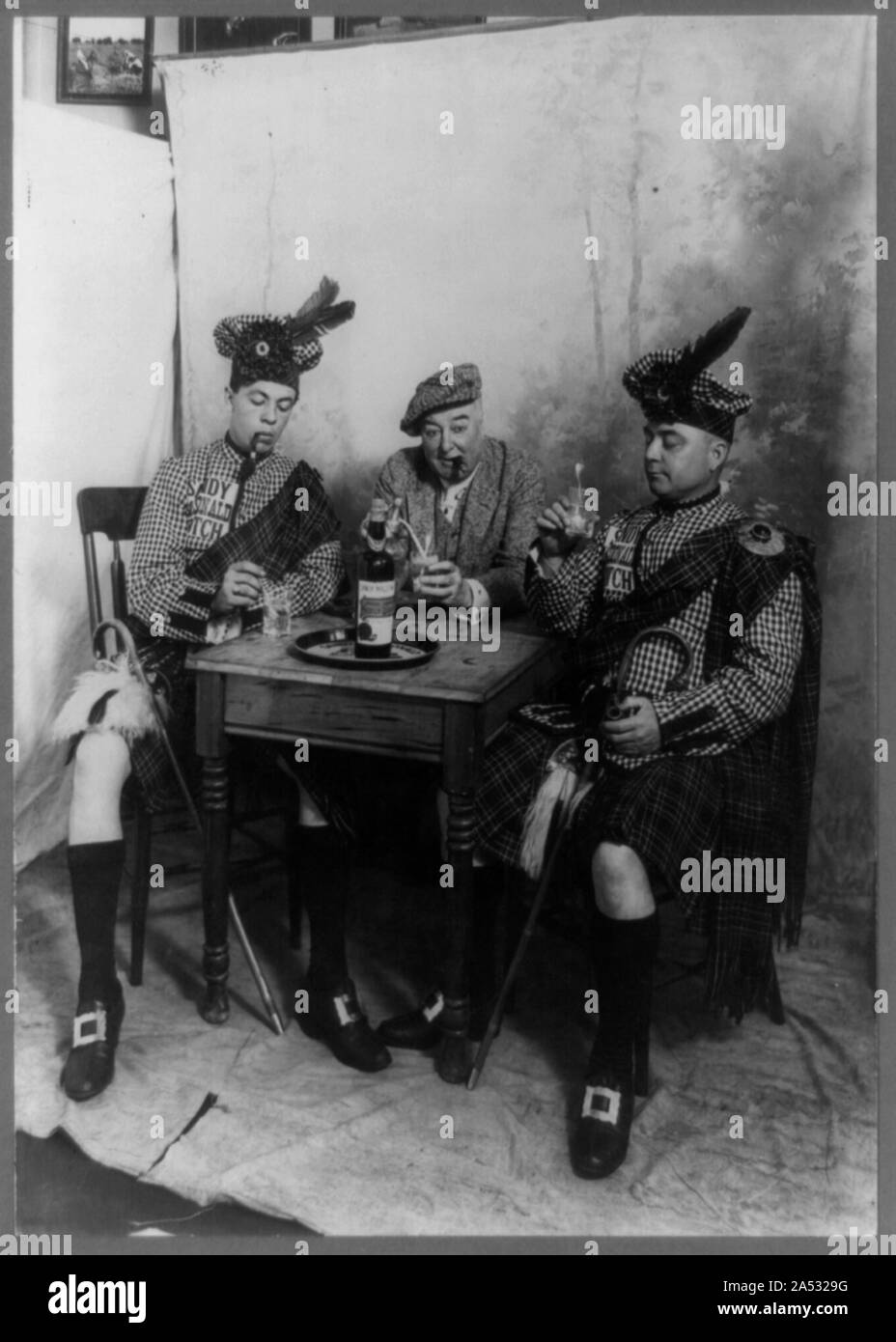 Two men wearing kilts and man smoking cigar, seated at small table drinking Sandy MacDonald scotch Stock Photo