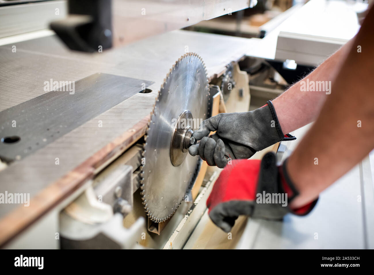 Carpenter adjusting the toothed round blade on a circular saw in a woodworking workshop in a close up on his gloved hands and the power tool Stock Photo