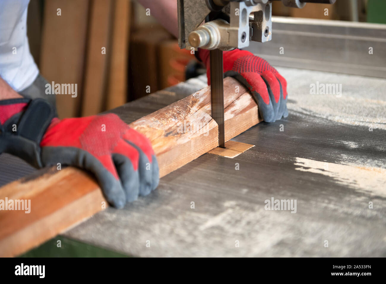 Carpenter cutting wood on a band saw on a workbench in a woodworking workshop in a close up on his hands and focus to the blade Stock Photo