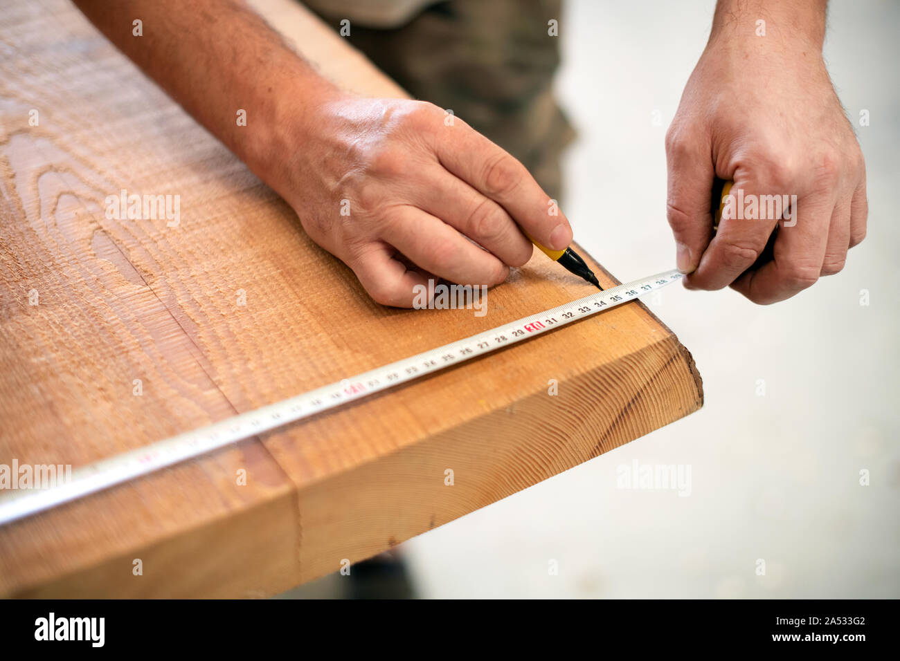 Carpenter measuring a wooden plank with a tape measure and marker in a woodworking workshop in a close up on his hands Stock Photo