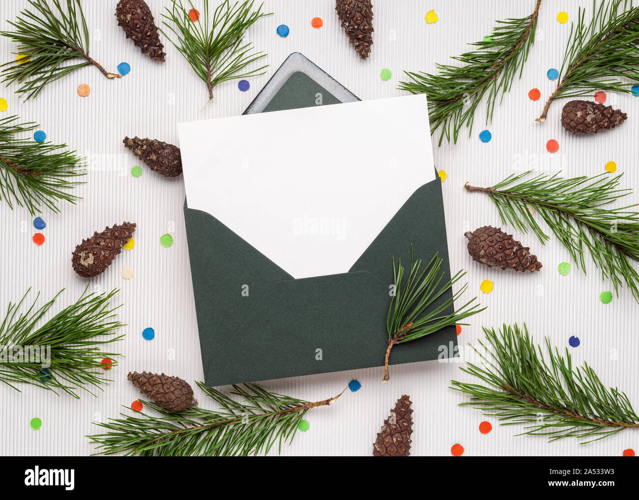 Merry Christmas and happy New Year card in envelope. White note paper sheet. Decor from pine branches, cones and festive confetti Stock Photo
