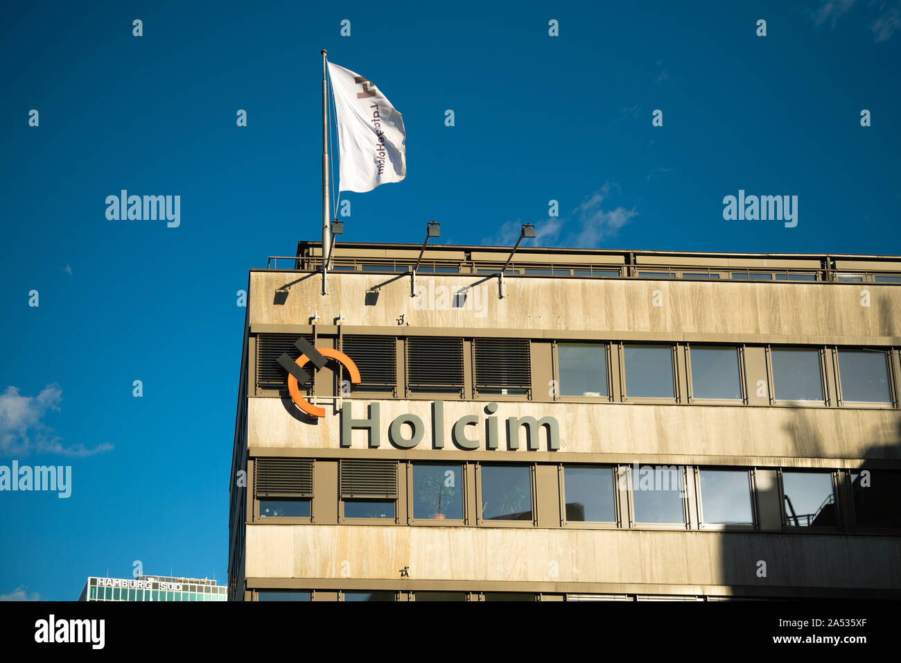 Hamburg Germany Mar 18 Front View Of Logotype Insignia On The Headquarter Of Holcim Swiss Based Global Building Materials And Aggregates Company With Waving Flag And Clear Blue Sky Stock Photo Alamy