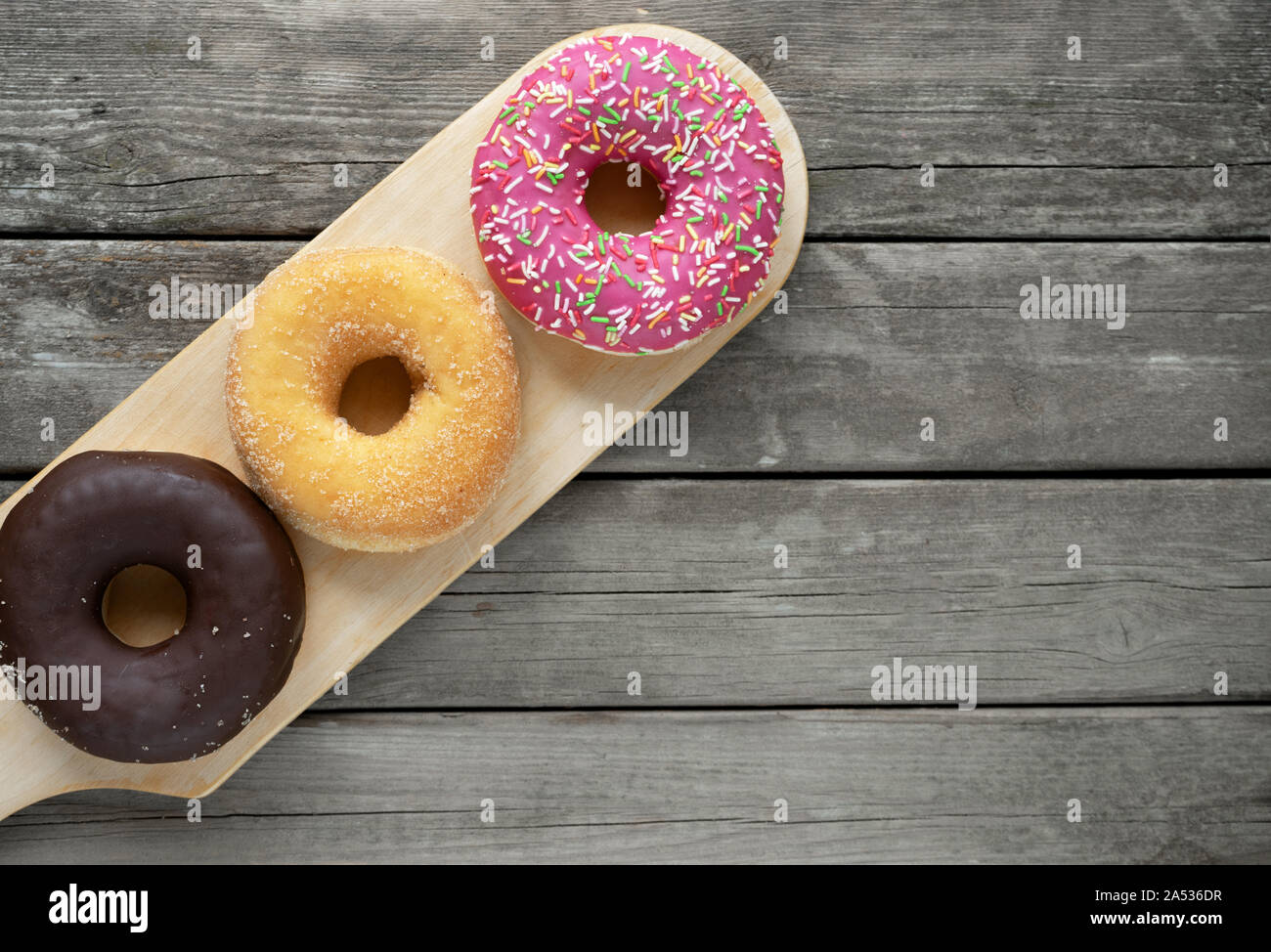 three donuts on a wooden board background with blank space Stock Photo