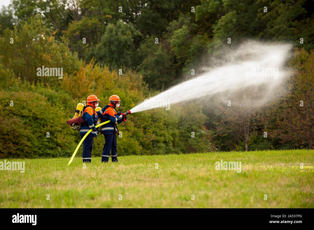 Germany, Niederstetten, Baden Wurttemberg. September 2019 Young firefighters in training with fire hose by extinguishing the fire. Stock Photo