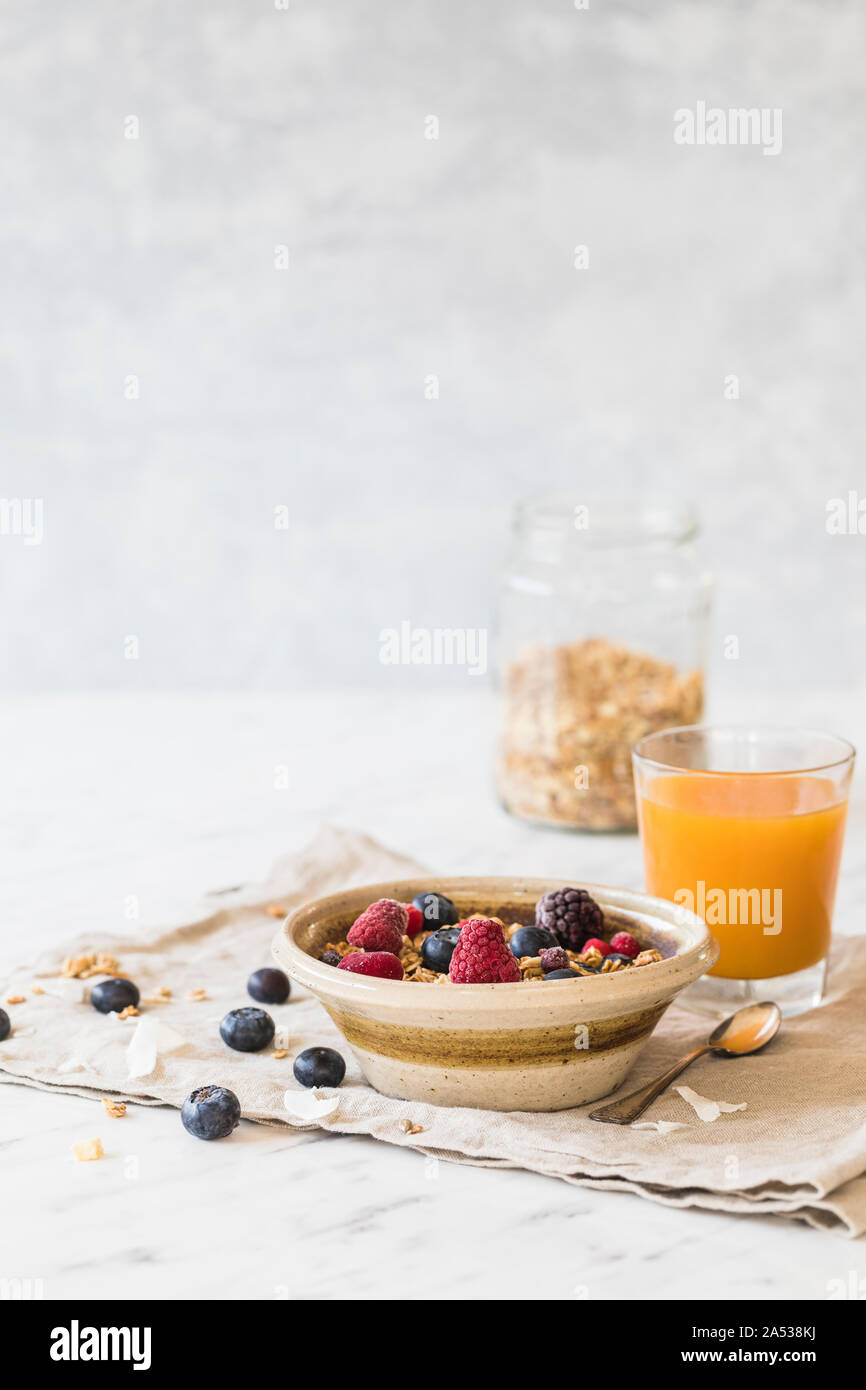 A fresh healthy breakfast with granola cereals, fresh berries - blueberries, raspberries. Orange juice, and a granola jar in the background.  Vertical Stock Photo