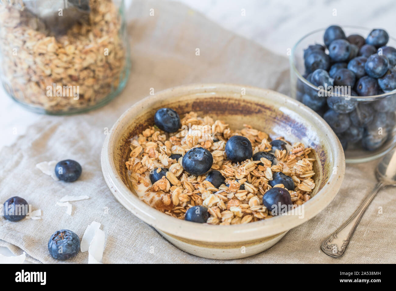 A fresh healthy breakfast with granola cereals, and fresh american blueberries.  There is a bowl of blueberries next to the granola bowl, and a glass Stock Photo