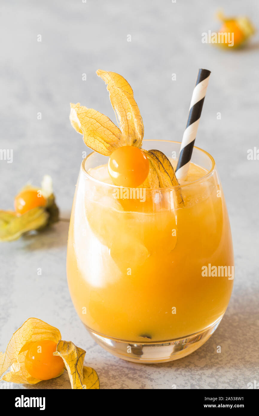 A orange drink decorated with physalis winter cherry and a black and white ribboned environmental friendly paper straw. There are some winter cherries Stock Photo