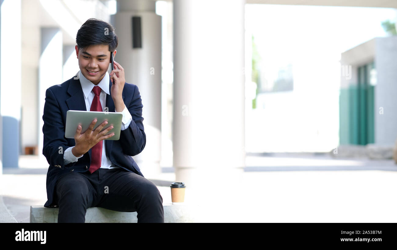 Young businessman in black suit speaking over mobile or smart phone with business partners. Business outdoors. Stock Photo