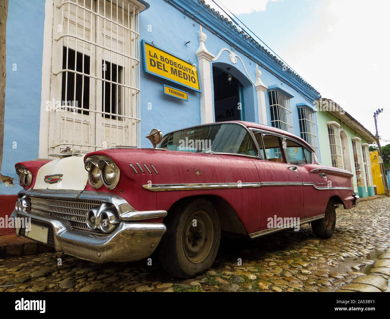 Old colorful Cuban car on cobblestone street, next to colonial houses Stock Photo
