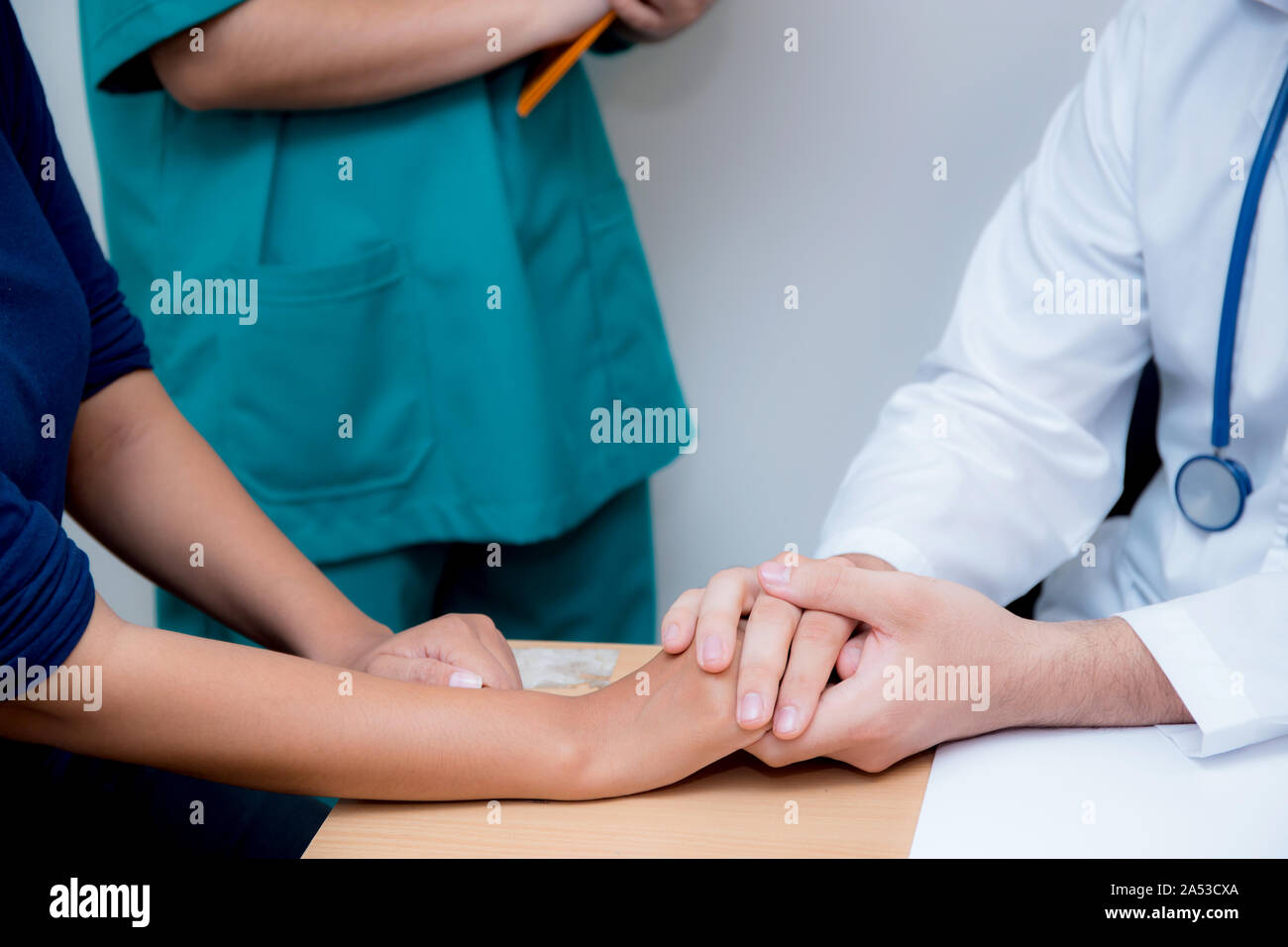 Friendly male doctor hand holding patient hand sitting at the desk for encouragement - empathy - cheering and support while medical examination. Stock Photo