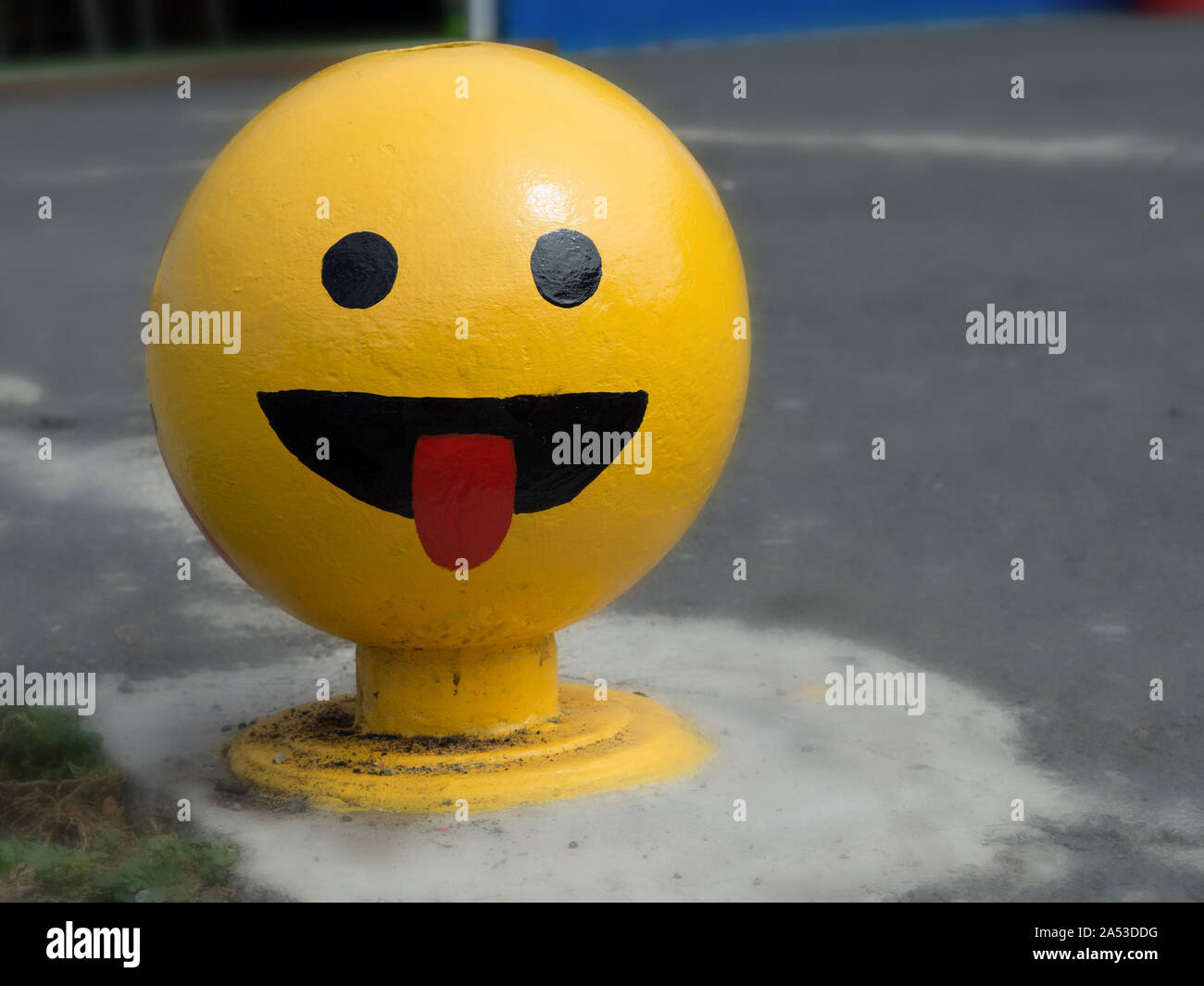 a big bright yellow ball-shaped Smily in the middle of a sidewalk sticks out his tongue  and laughs Stock Photo