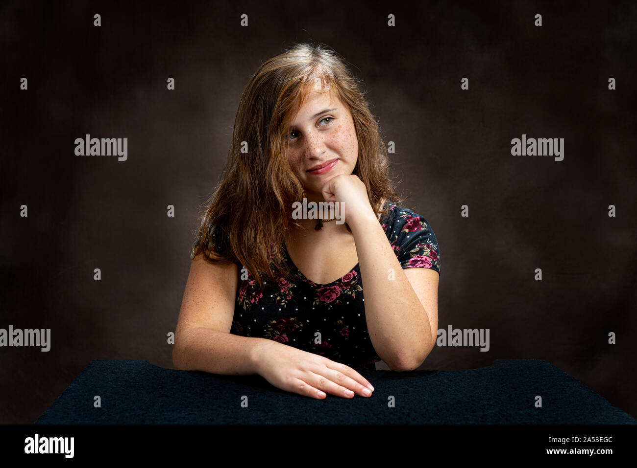 Horizontal studio shot of an amused pre-teen young lady listening to someone talk.  Her head is resting on her hand and is slightly tilted to one side Stock Photo