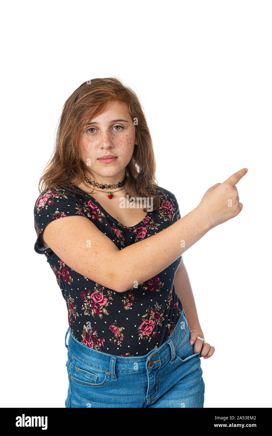 Vertical studio shot of a re-teen girl with freckles pointing to the right with her right hand.  Serious expression.  White background with copy space Stock Photo