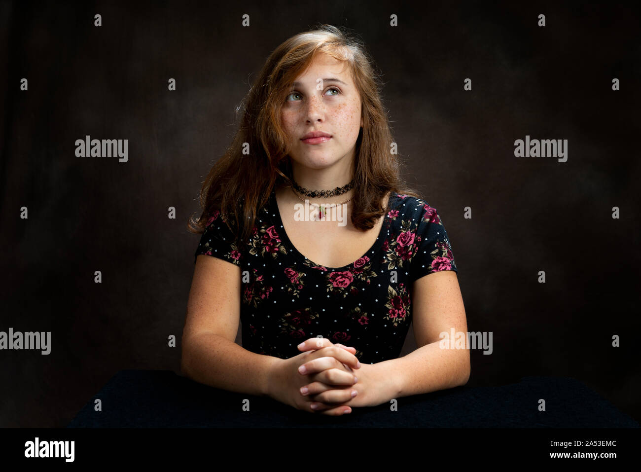 Horizontal studio shot of a pre-teen young lady with her hands clasped looking up and praying.  Brown background with copy space. Stock Photo