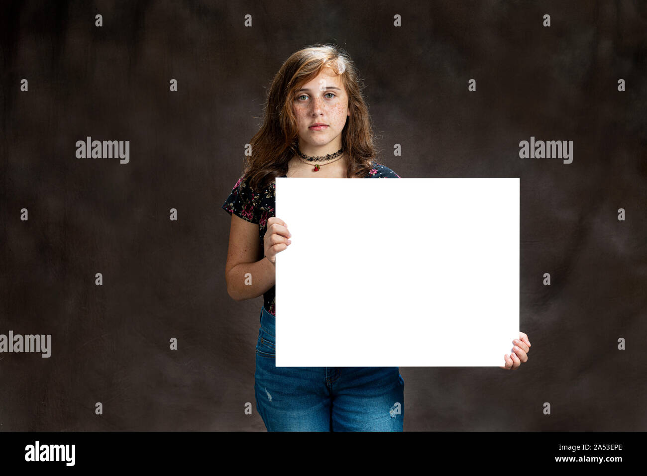 Horizontal studio shot of a serious looking pre-teen girl with freckles holding a blank white sign.  Brown background.  Copy space. Stock Photo