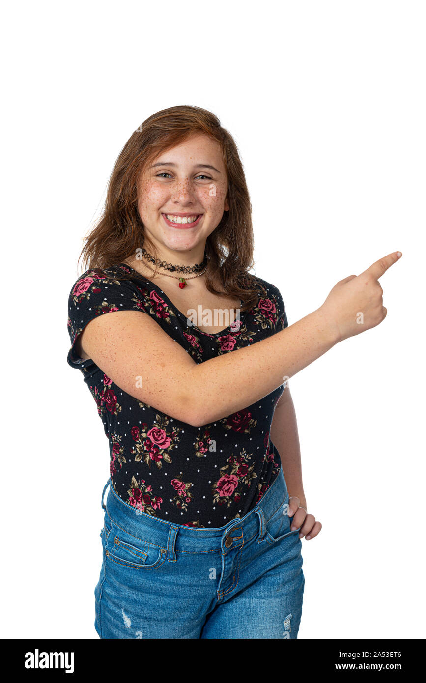 Vertical studio shot of a smiling re-teen girl with freckles pointing to the right across her body with her right hand.  White background with copy sp Stock Photo