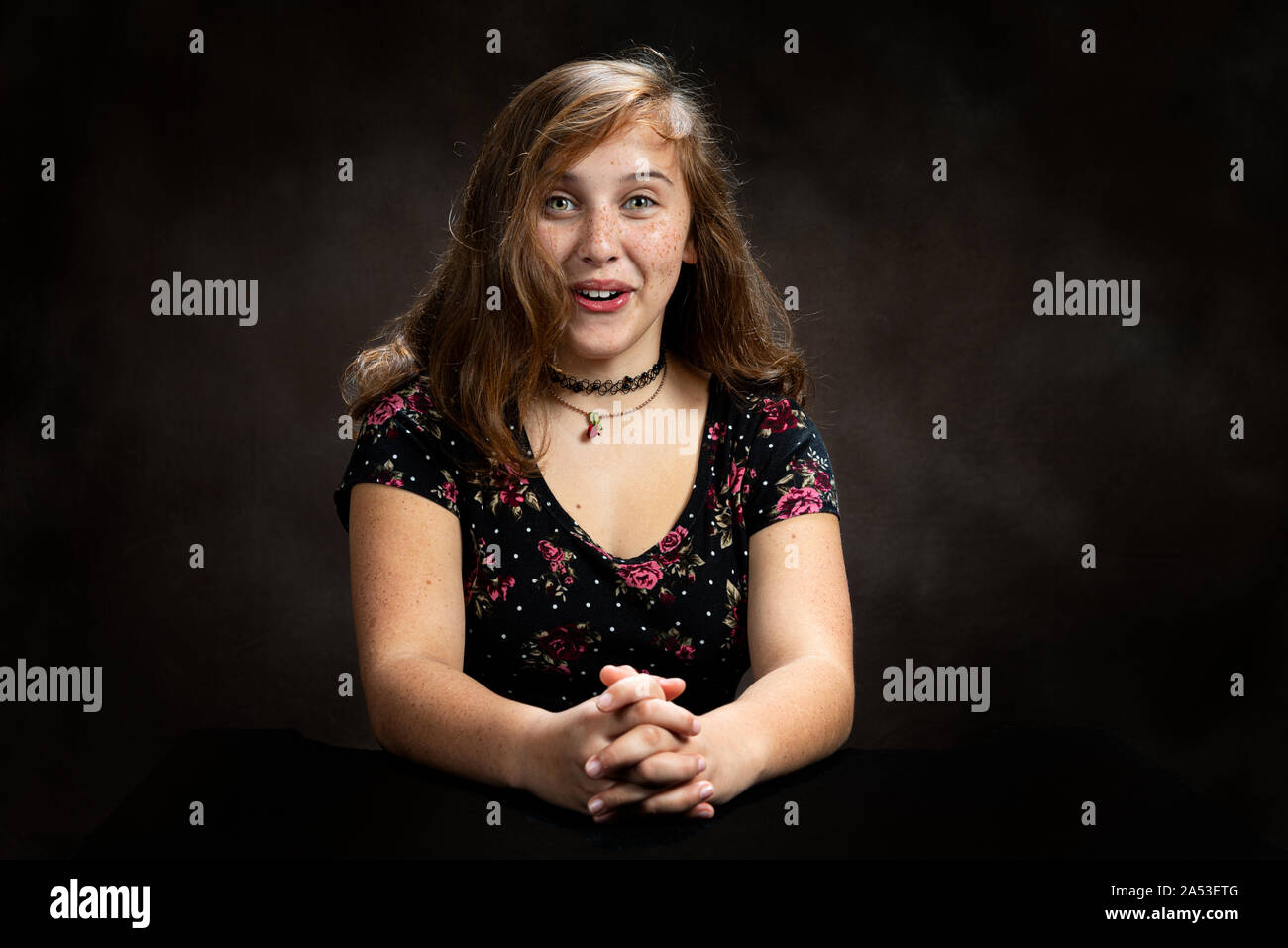 Horizontal studio shot of a surprised and amused pre-teen girl.  Brown background.  She is sitting down.  Shot is from the waist up. Stock Photo