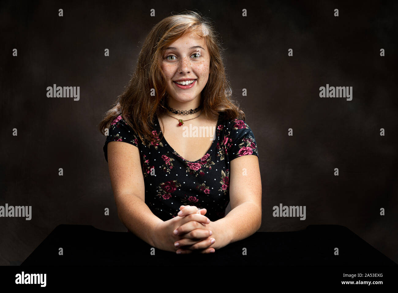 Horizontal studio shot of a very happy and excited pre-teen girl.  Brown background.  She is sitting down.  Shot is from the waist up. Stock Photo