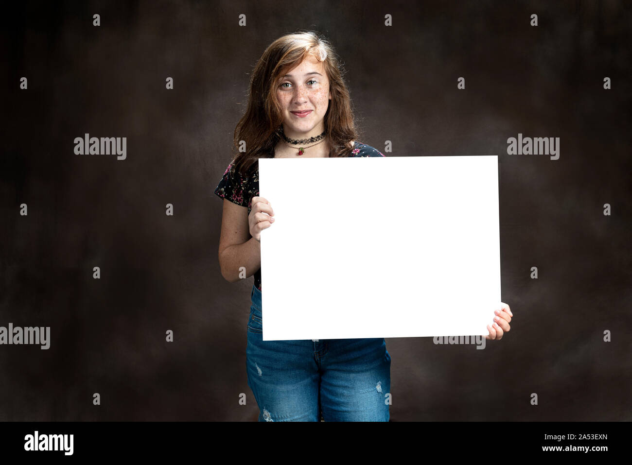 Horizontal shot of an amused pre-teen girl with freckles holding a blank sign. Stock Photo