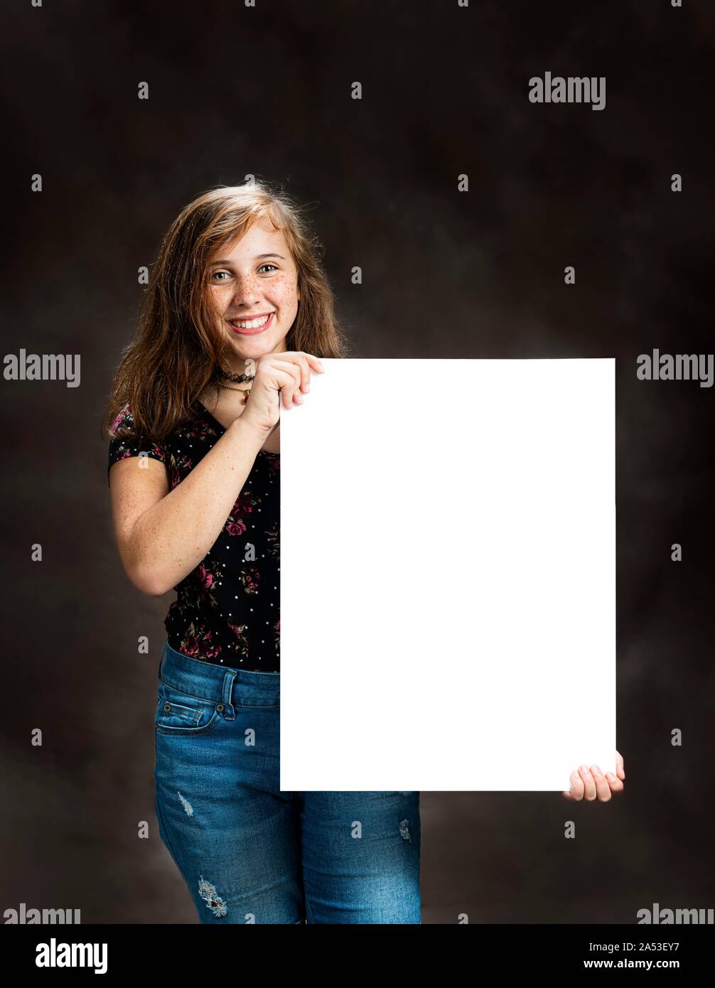 Vertical shot of a cute pre-teen girl holding a blank sign. Stock Photo