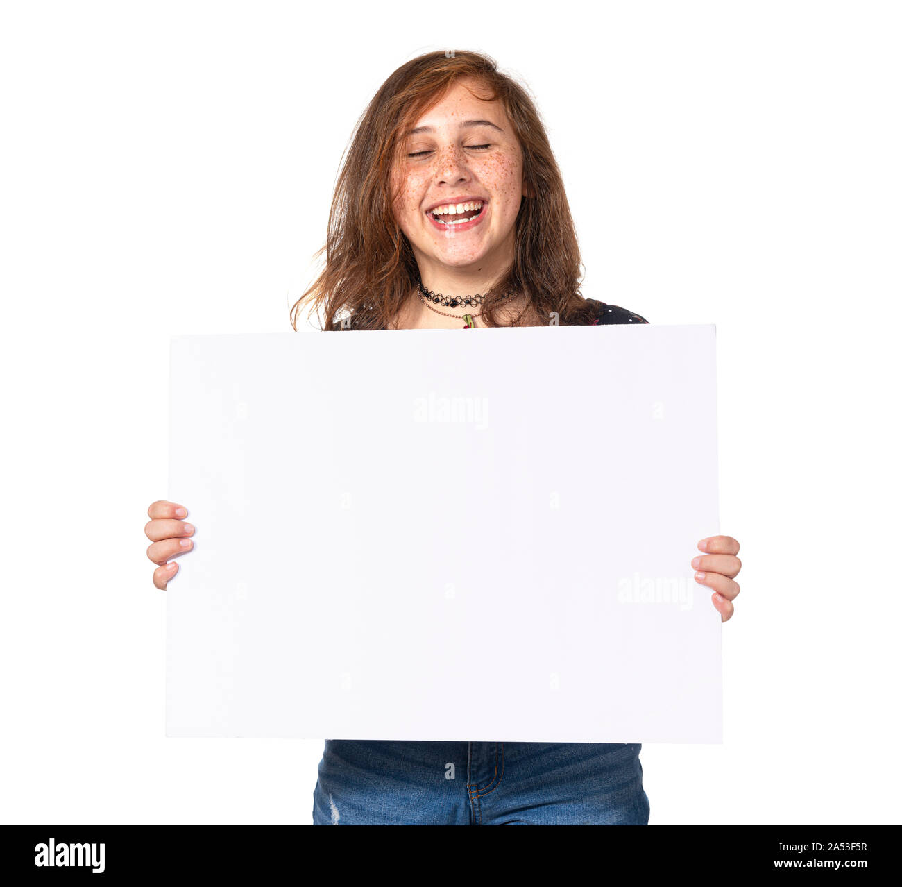 Horizontal studio shot of a laughing pre-teen girl holding a blank white sign isolated on white. Stock Photo
