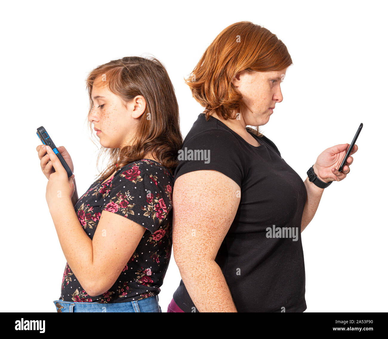 Horizontal studio shot of a mother and daughter leaning back to back each using her own cell phone.  White background. Stock Photo