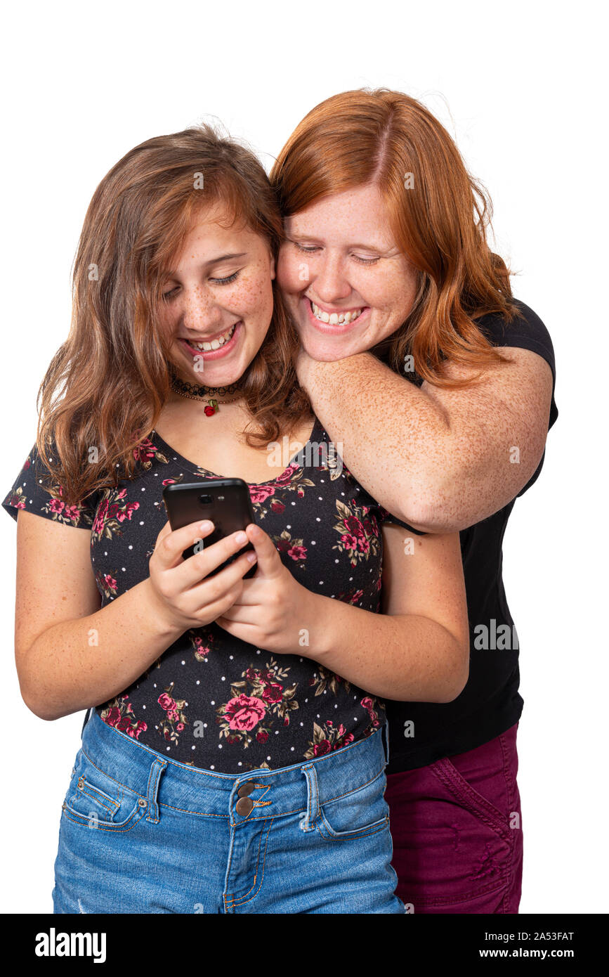 Vertical studio shot of a mother leaning on her daughter’s shoulder watching her use her cell phone.  They are both laughing.  White background. Stock Photo