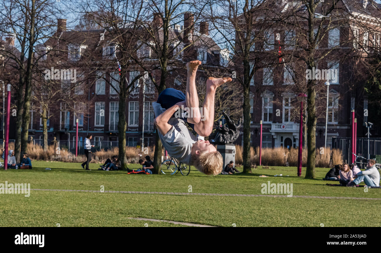 Amsterdam, Holland, February 25 2019 street flipping boy on the grass of the Museumplein in Amsterdam in his shorts on a sunny day Stock Photo