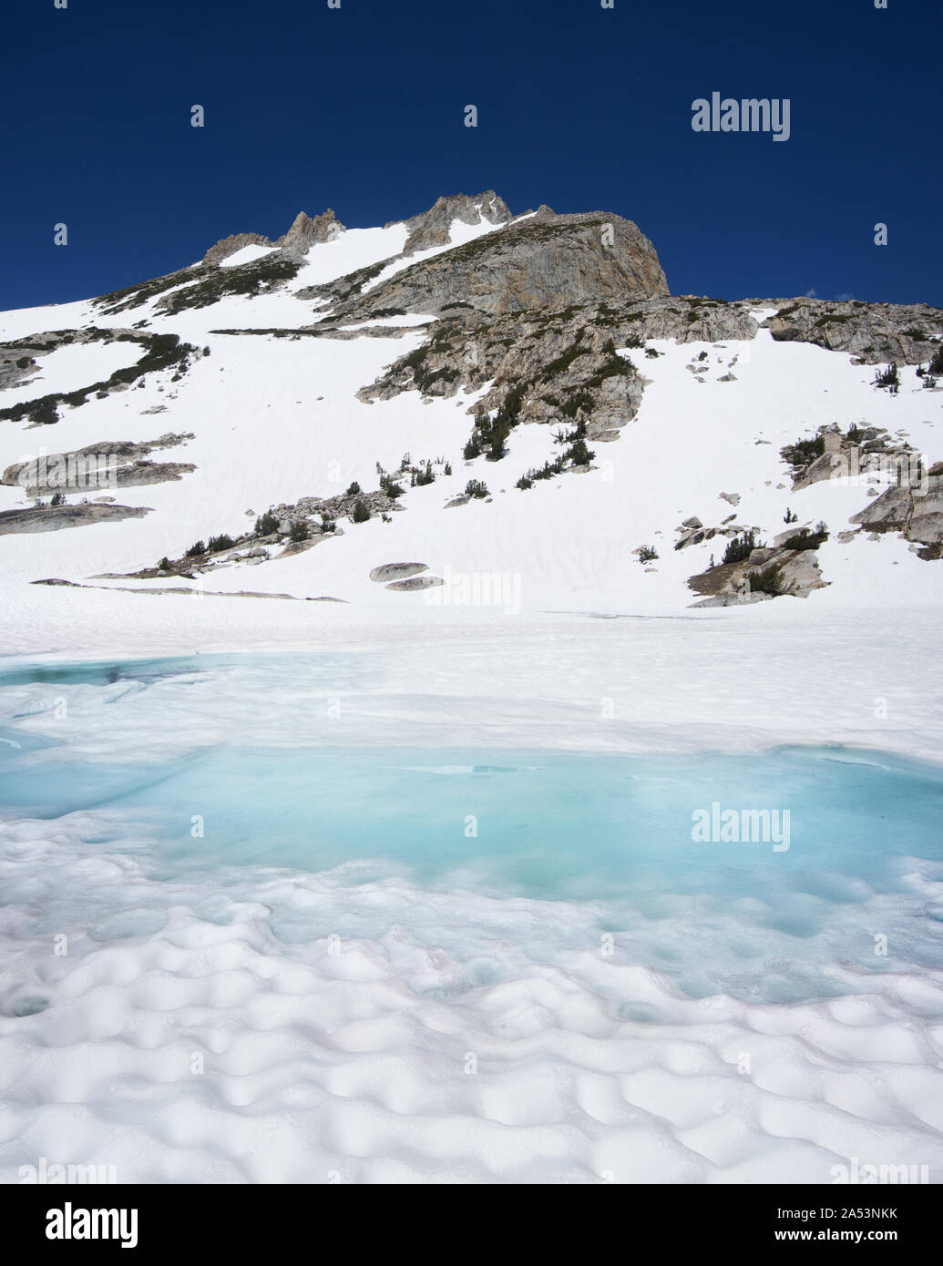 North Peak rises above a snowy but starting to melt lake near Tioga Pass in the Sierra Nevada Mountains Stock Photo