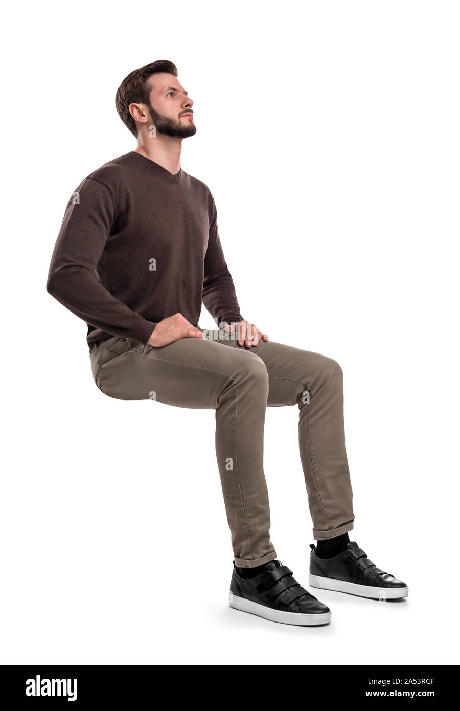 An isolated bearded man in casual wear sits on a white background with ...