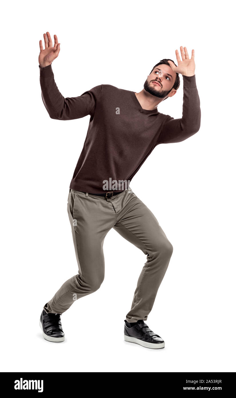A bearded man in casual garb stands cowering under something dangerous above him. Stock Photo