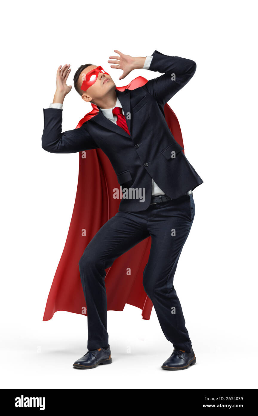 A businessman in a hero red cape and a mask in front view crouching in fear on white background. Stock Photo